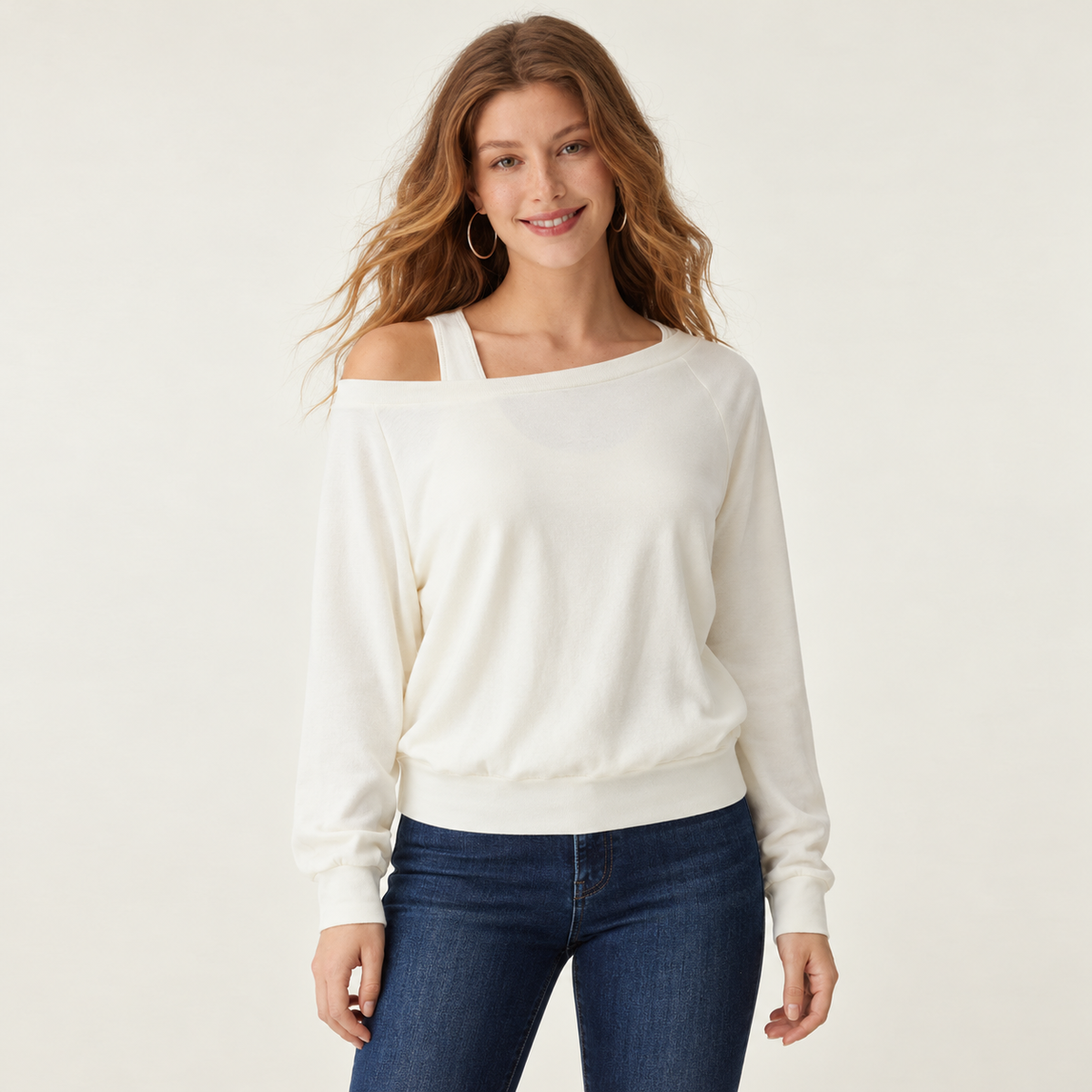 Top de manga larga blanco hueso en uso, con tirante integrado visible y detalle de capas en una sola prenda; jeans de ambientación no incluidos.